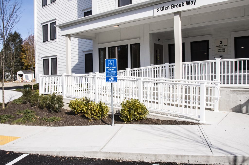 New construction: from edge of parking lot with handicap spots, a view of an apartment building with an attractive ramp to the entrance.